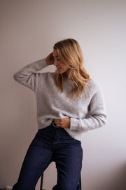 Pull dos ouvert à nœud porté par une femme, vue de trois-quarts, main dans les cheveux, jean foncé