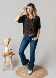 Pull fin col V léopard porté par une femme, silhouette entière, jean flare, tabouret