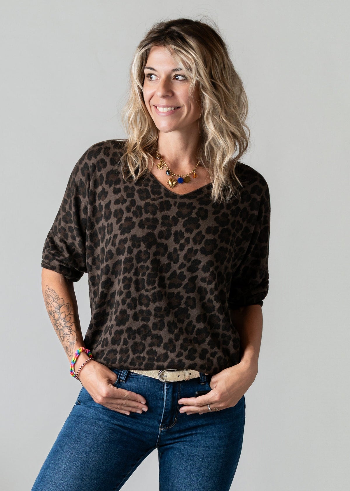 Pull fin col V léopard porté par une femme, vue de trois-quarts, mains dans les poches, fond gris