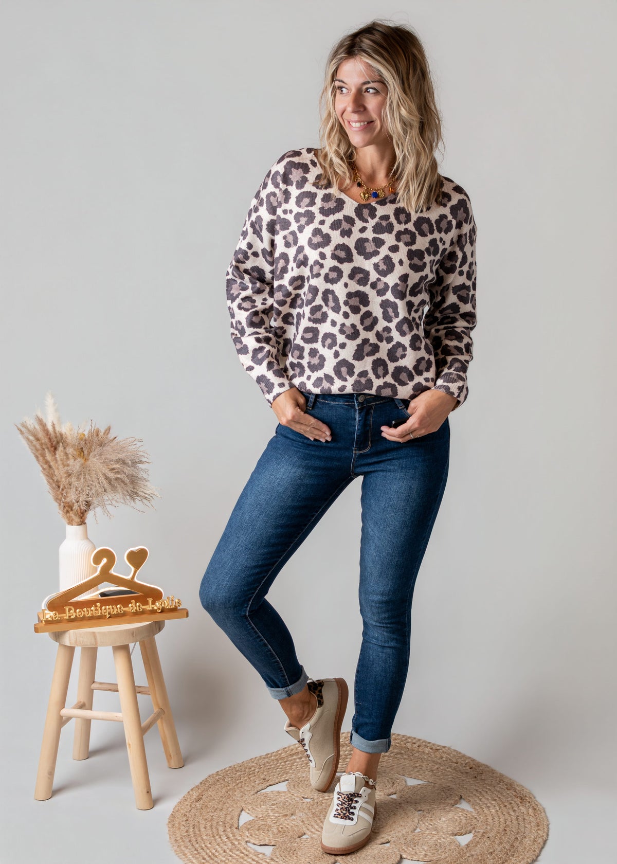 Pull léopard à col V porté par une femme, silhouette entière, jean, tabouret