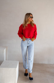 Pull col rond porté par une femme, silhouette entière, jean clair, escarpins noirs, mur blanc