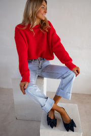 Pull col rond porté par une femme, assise, sur un cube blanc, jambes croisées