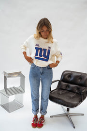Pull à logo manches longues écru porté par une femme, vue de face, fauteuil noir, baskets rouges