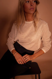 Pull à paillettes col rond porté par une femme, vue rapprochée, pantalon noir, mains jointes