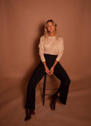 Pull à paillettes col rond porté par une femme, assise, sur un tabouret, pantalon évasé noir