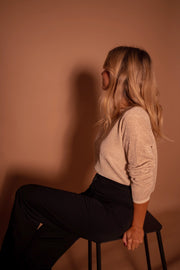 Pull à paillettes col rond porté par une femme, assise, sur un tabouret, de profil