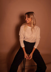 Pull à paillettes col rond porté par une femme, assise, sur un tabouret, sourire