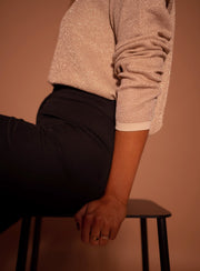 Pull à paillettes col rond porté par une femme, gros plan de la manche et du pantalon noir