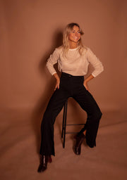 Pull à paillettes col rond porté par une femme, silhouette entière, pantalon évasé noir, bottines, tabouret