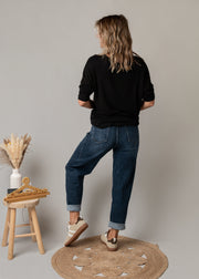 Jean en denim coupe arrondie porté par une femme, vue de dos, t-shirt noir, jambe repliée