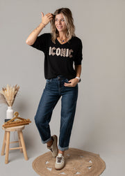 Jean en denim coupe arrondie porté par une femme, vue de trois-quarts, t-shirt noir à lettres, tabouret