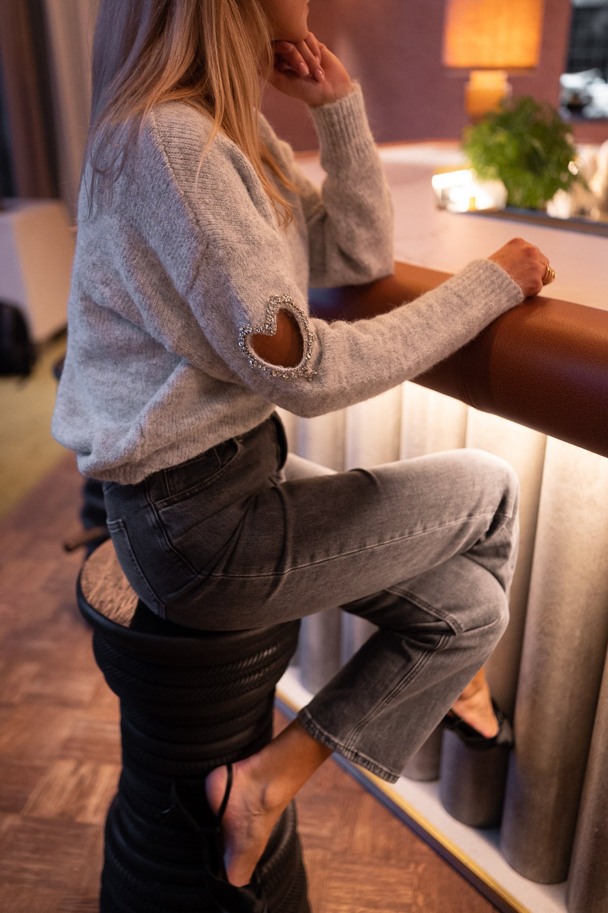 Pull à ouvertures strassées porté par une femme, vue de profil, bar, tabouret, jean noir