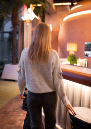 Pull à ouvertures strassées porté par une femme, vue de dos, cheveux longs, bar