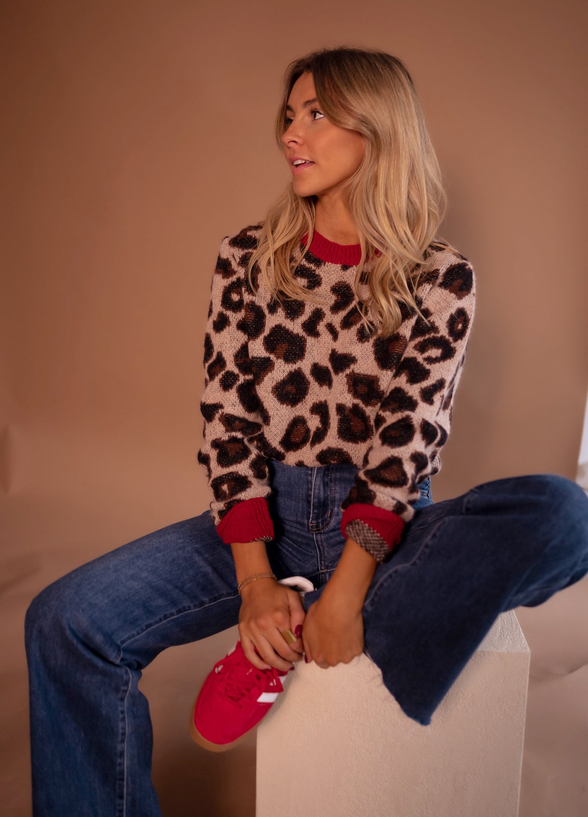 Pull doux à motif léopard porté par une femme, assise, sur un cube blanc, jean, baskets rouges