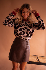 Pull doux à motif léopard porté par une femme, vue rapprochée, mains dans les cheveux, jupe en cuir