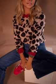 Pull doux à motif léopard porté par une femme, assise, cube blanc, jean, baskets rouges, sourire