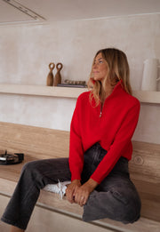 Pull rayé col montant zippé porté par une femme, assise, sur un plan de travail, jean noir