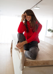 Pull rayé col montant zippé porté par une femme, assise, sur un plan de travail, sourire
