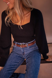 Pull à manches légèrement bouffantes porté par une femme, vue rapprochée, ceinture marron, jean