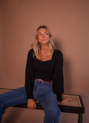 Pull à manches légèrement bouffantes porté par une femme, assise, sur un banc en cannage, jean