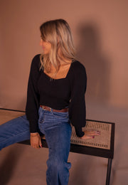 Pull à manches légèrement bouffantes porté par une femme, assise, sur un banc, de profil