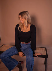 Pull à manches légèrement bouffantes porté par une femme, assise, sur un banc, jean, regard sur le côté
