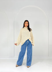 Pull bouclé beige — vue portée en pied, jean large clair, sous une arche blanche