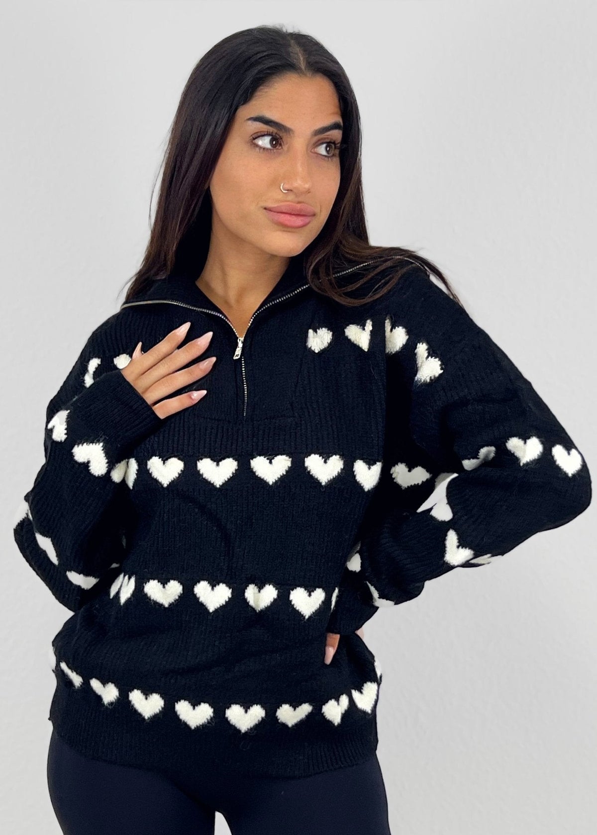 Pull à fermeture zippée noir — vue portée de face, cadrée à la taille, col entrouvert, petits cœurs blancs