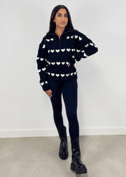Pull à fermeture zippée noir — vue portée en pied, pantalon noir et bottines, main sur la hanche