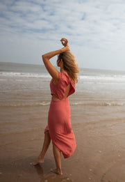 Robe longue col montant fendue portée par une femme, vue de trois-quarts, main dans les cheveux, plage