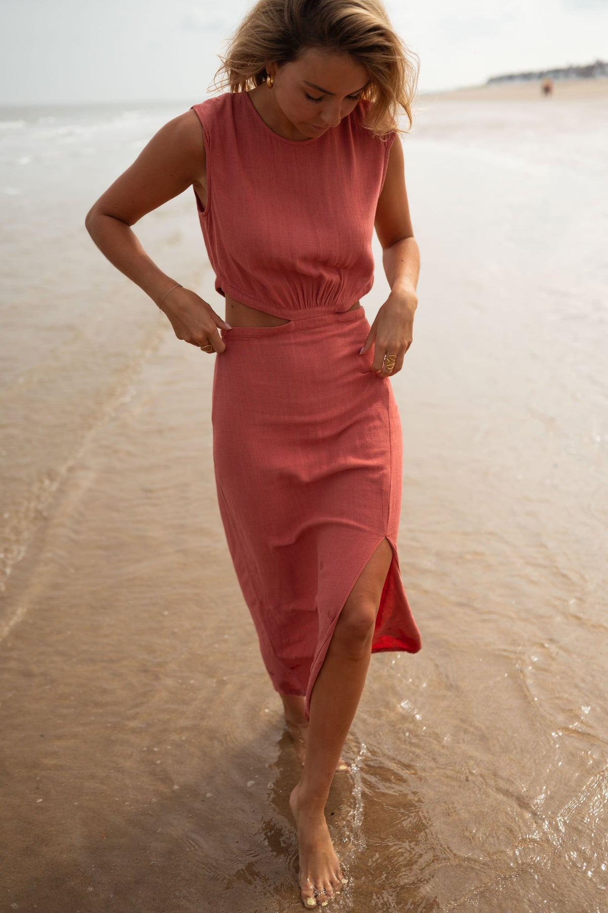 Robe longue col montant fendue portée par une femme, vue de face, plage, mains sur les hanches