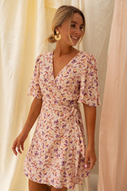 Robe fleurie cache-cœur courte portée par une femme, vue de trois-quarts, rideaux, mains sur la taille
