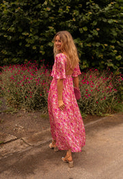 Robe fleurie à dos ouvert portée par une femme, vue de dos, allée, fleurs roses