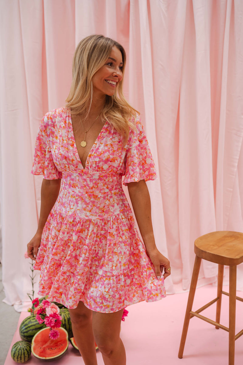 Robe fleurie à manches courtes portée par une femme, vue de face, rideau rose, pastèques