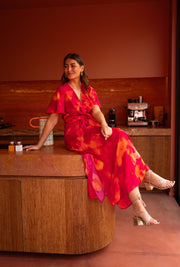 Robe longue col V fendue portée par une femme, assise, îlot en bois, jambes croisées