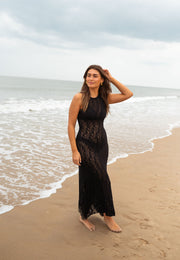 Robe crochet longue dos ouvert portée par une femme, vue de trois-quarts, main dans les cheveux, mer