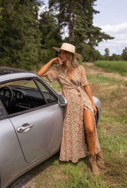 Robe portefeuille fleurie fluide portée par une femme, vue de face, voiture grise, chapeau de paille