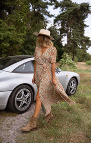 Robe portefeuille fleurie fluide portée par une femme, en marchant, voiture grise, chapeau