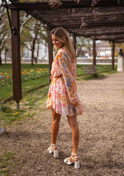 Robe fleurie à manches transparentes portée par une femme, vue de face, pergola, sandales blanches
