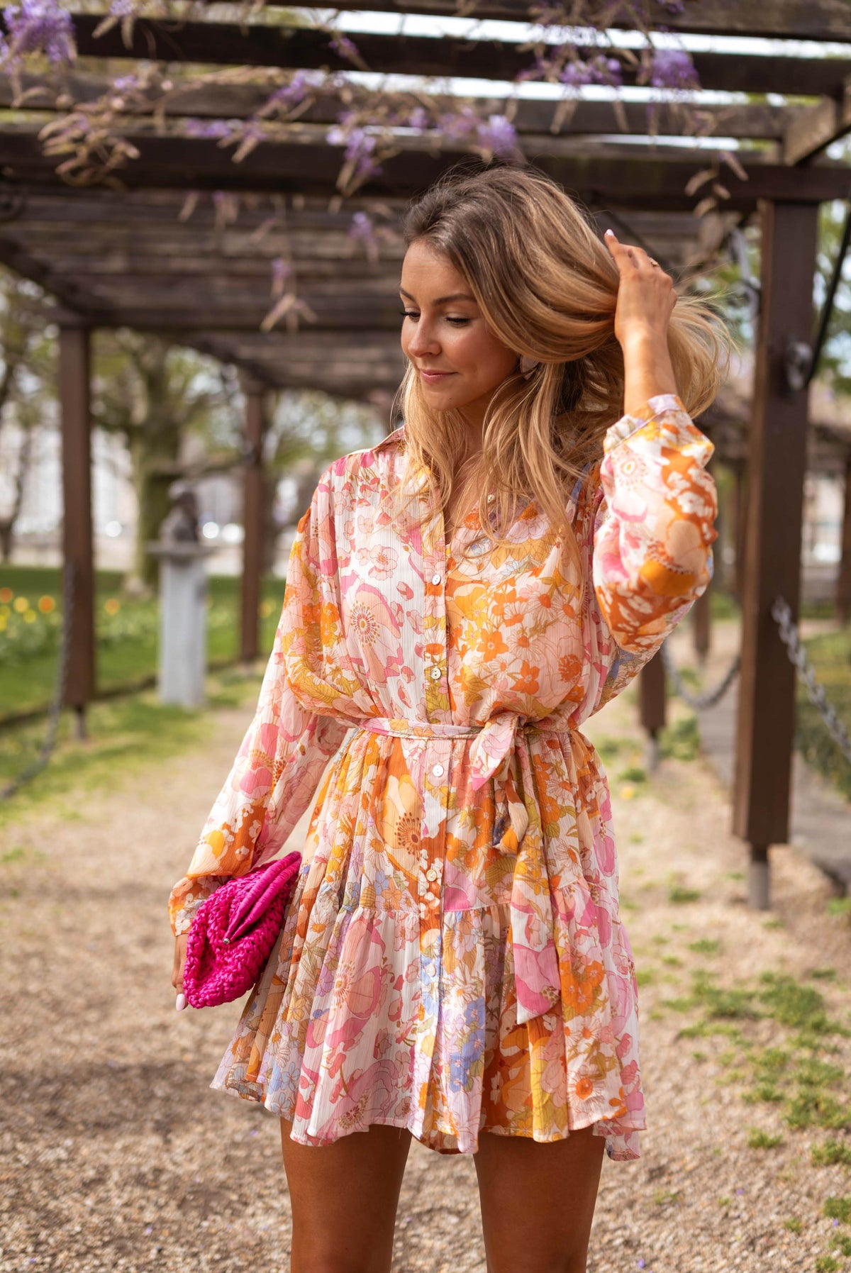 Robe fleurie à manches transparentes portée par une femme, vue de face, pergola, pochette rose