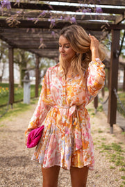 Robe fleurie à manches transparentes portée par une femme, vue de face, pergola, pochette rose