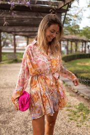 Robe fleurie à manches transparentes portée par une femme, vue de face, chemin, pochette fuchsia