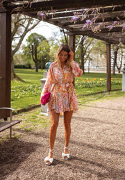 Robe fleurie à manches transparentes portée par une femme, vue de face, pelouse, pochette rose
