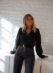 Blouse transparente à col V portée par une femme, silhouette entière, jean gris, mur blanc