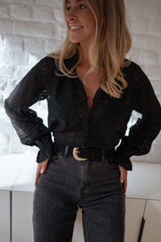 Blouse transparente à col V portée par une femme, vue de trois-quarts, ceinture, mur blanc