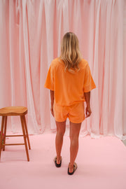 Short éponge à cordon porté par une femme, silhouette entière, rideaux roses, tabouret
