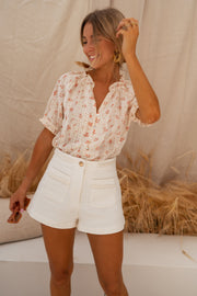 Short doublé effet tweed porté par une femme, vue de face, chemisier fleuri, sourire