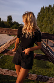 Short court effet tweed porté par une femme, silhouette entière, barrière en bois, t-shirt noir