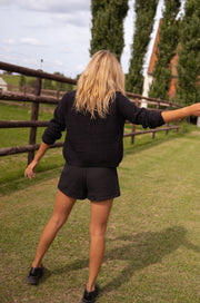 Short court effet tweed porté par une femme, vue de dos, barrière, haut noir