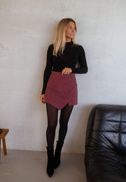 Jupe-short à carreaux drapée porté par une femme, silhouette entière, haut noir, collants